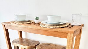 Une table de salle à manger en bois, accompagnée de deux tabourets, d’assiettes blanches et d’une petite plante en pot.