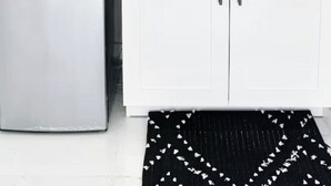 Une cuisine moderne avec des armoires blanches, un réfrigérateur en acier inoxydable, une cuisinière à gaz et une serviette rayée noire et blanche accrochée au mur.