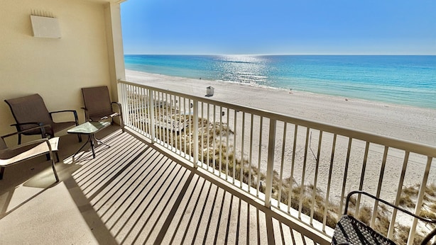 A balcony with two chairs and a small table, overlooking a beach with clear blue water and a sandy shore. - Beachfront Studio w/ Bunks Sleeps 4 at Majestic! (Panama City Beach)