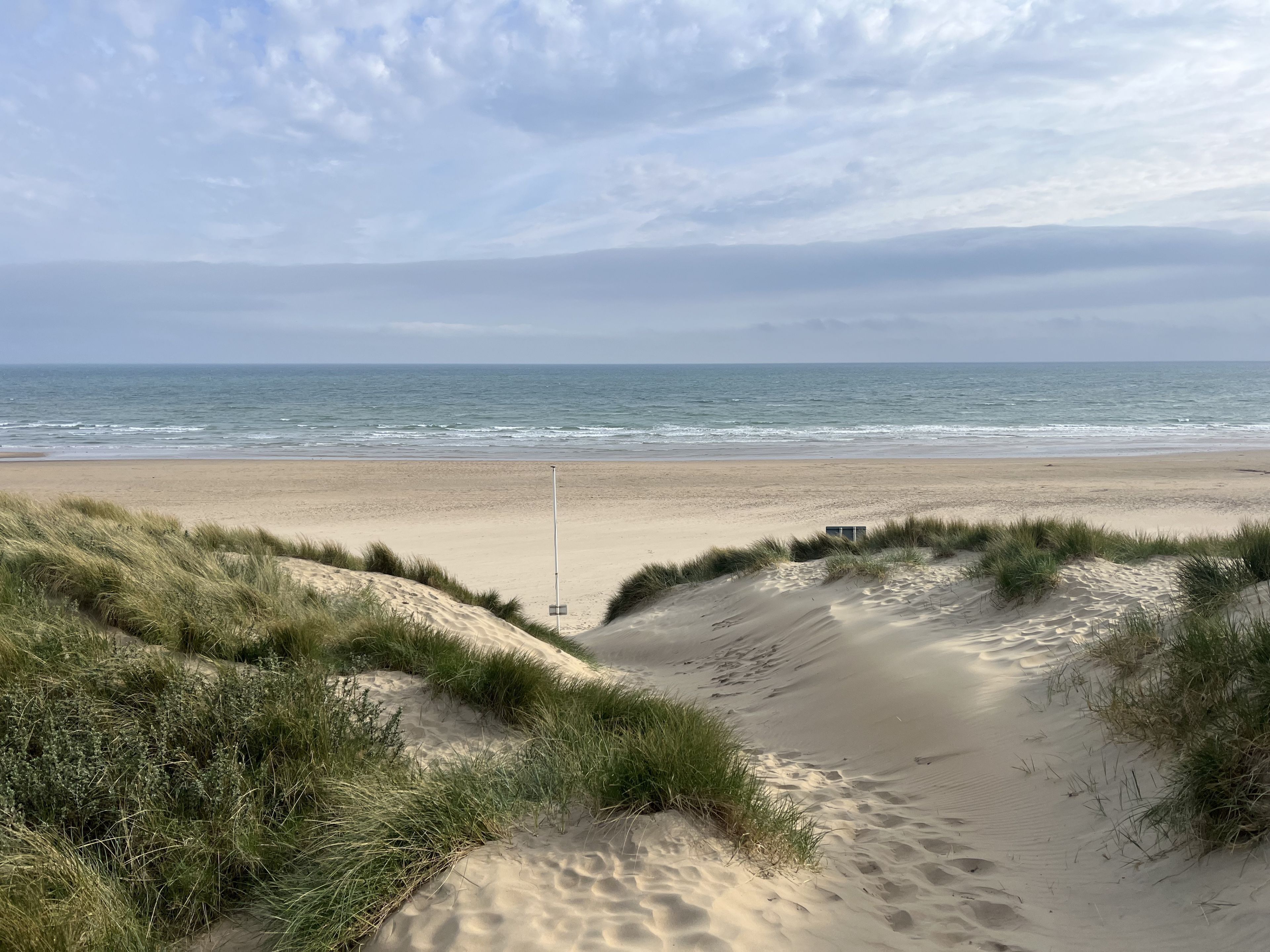 Une plage avec des dunes de sable et un mât de drapeau au centre.