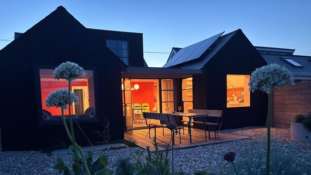 Et moderne hus med træterrasse, spiseområde og et synligt køkken.
