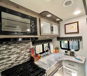 A compact RV kitchen with a built-in microwave, a sink, and a stove. - Warm-n-Toasty Camper in the City / BRING THE DOG! (Decatur)
