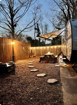 A covered outdoor area with a fire pit, seating, and a wooden fence. - Warm-n-Toasty Camper in the City / BRING THE DOG! (Decatur)
