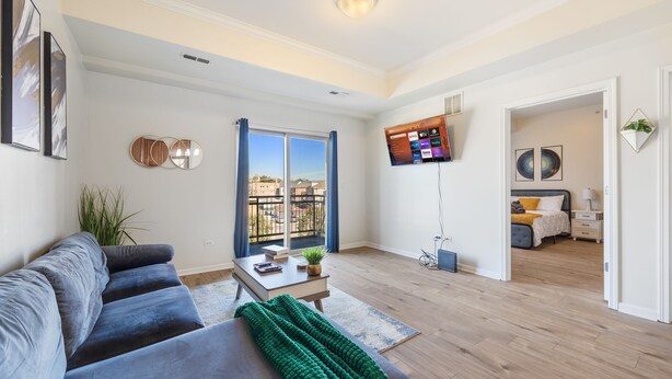 A modern living room with a grey sofa, a coffee table, and a TV mounted on the wall. - Chic Elevator Apt mins to DT, Train, Dining & Hosp (Berwyn)