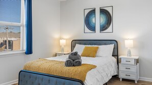 A bedroom with a bed, two bedside tables, a window with blinds, and two wall-mounted artworks. - Chic Elevator Apt mins to DT, Train, Dining & Hosp (Berwyn)