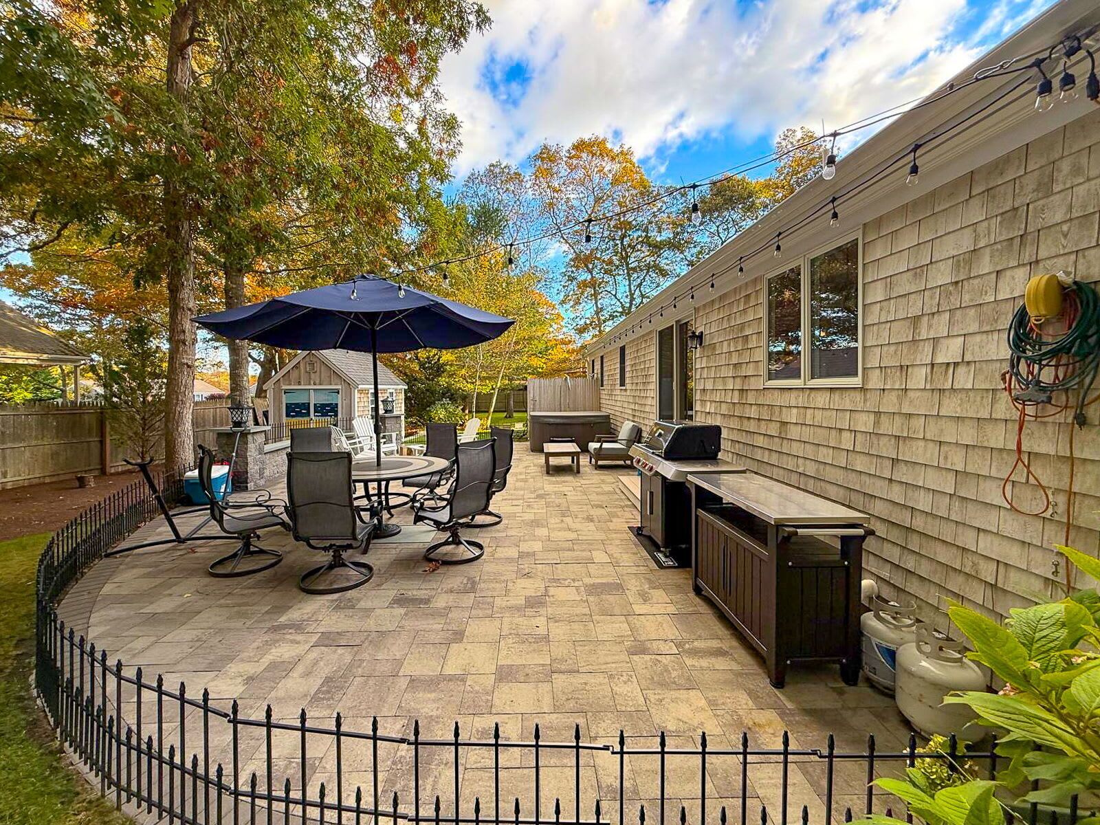 A patio area with a round table and chairs, a grill, and a covered seating area under an umbrella.