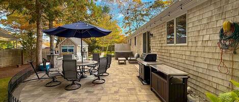 A patio area with a round table and chairs, a grill, and a covered seating area under an umbrella.