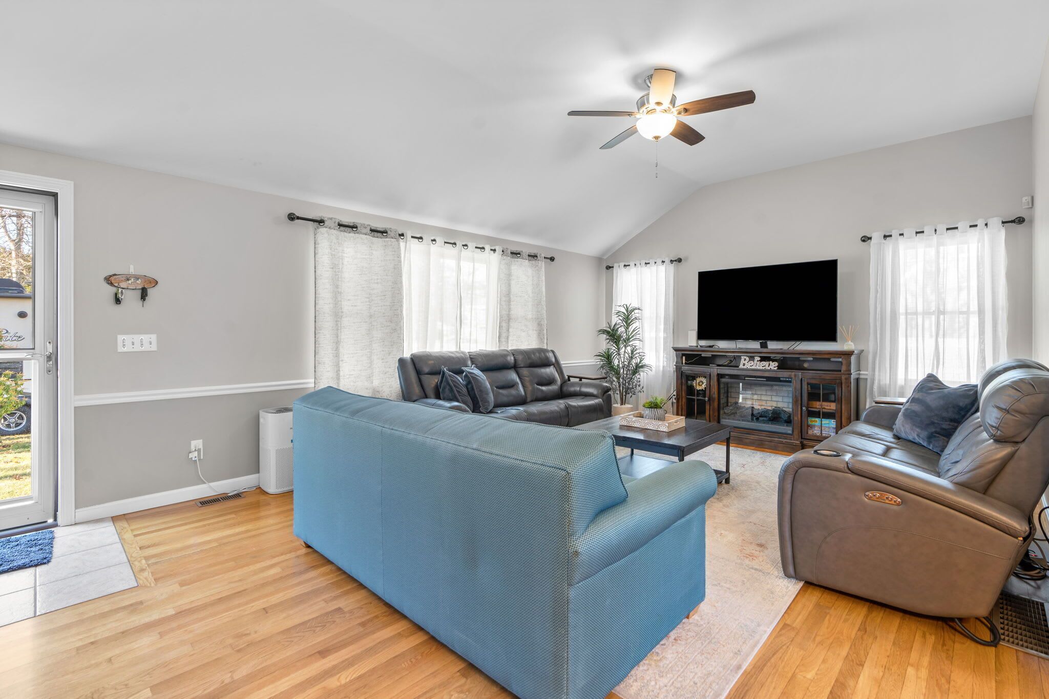 A spacious living room with a blue sofa, a brown leather recliner, a flat-screen TV, and a ceiling fan.
