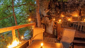 Terraza de madera al aire libre con una chimenea, asientos y un muro de piedra de fondo.