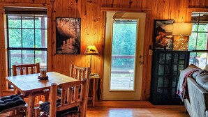 Un interior de madera con una mesa de comedor y sillas, una puerta con vistas, y una lámpara en un estante.