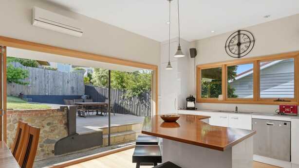 A modern kitchen with a large island, bar stools, and a view of the backyard. - Poets View - 3 Bedroom House (West Hobart)