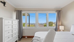 A bedroom with a bed, a dresser, a window with curtains, and a lamp. - Poets View - 3 Bedroom House (West Hobart)