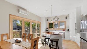 A modern kitchen with a central island, wooden dining table, and chairs. - Poets View - 3 Bedroom House (West Hobart)