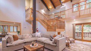 A spacious living area with a large sectional sofa, a wooden coffee table, and a staircase leading to an upper level. - Spacious 5BR Carnelian Grand Retreat, Hot Tub, perfect for the whole family (Carnelian Bay)