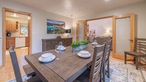 A dining area with a wooden table set for four, surrounded by chairs. There is a kitchen visible in the background, and a painting on the wall. - Spacious 5BR Carnelian Grand Retreat, Hot Tub, perfect for the whole family (Carnelian Bay)
