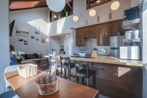 A modern kitchen with wooden cabinets, a central island, and pendant lighting. - 2BR + Loft Condo One Block from the Base Area, Deck View of the Lodge, Sleeps 6 (Angel Fire)