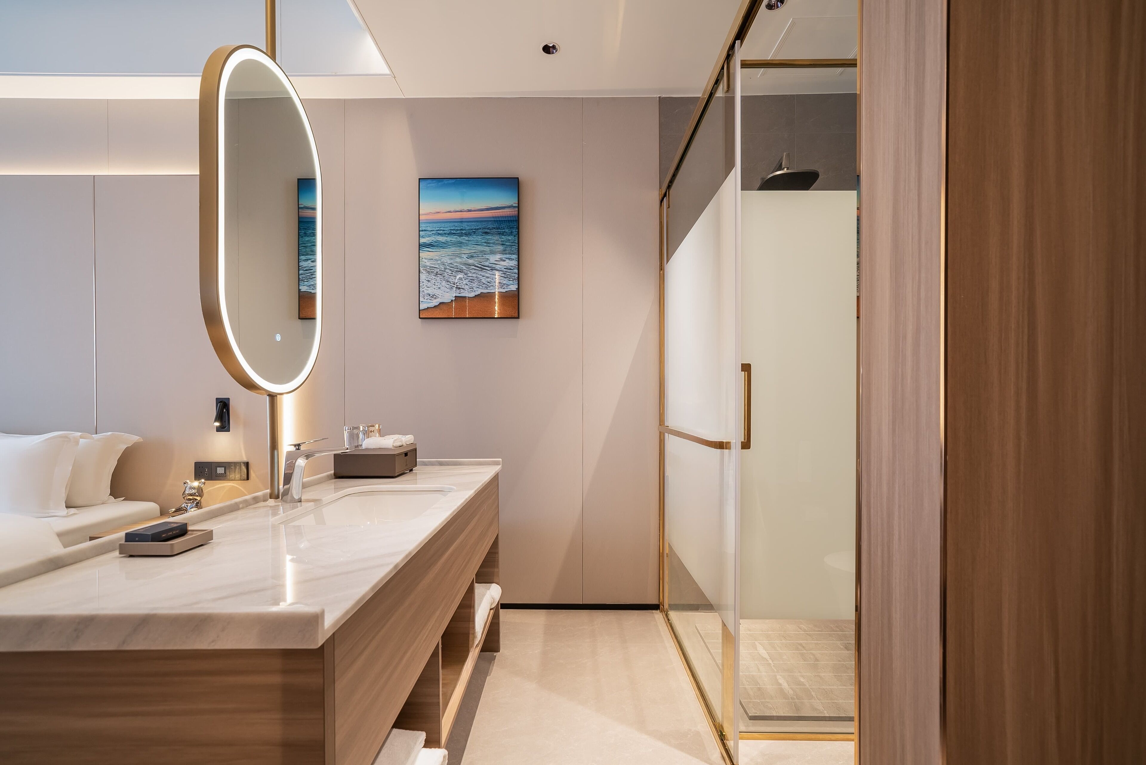 Une salle de bain moderne avec un grand miroir, un meuble-lavabo en bois, un tableau représentant une plage et une cabine de douche en verre.