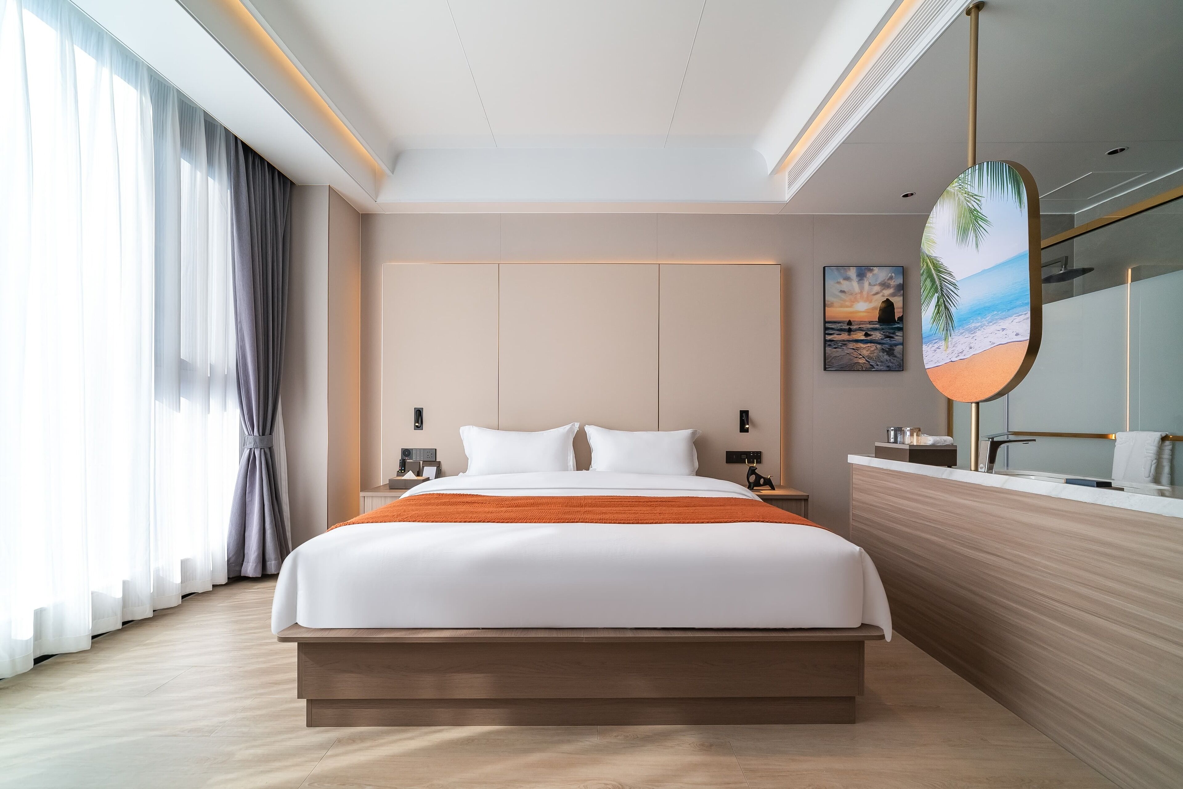 Una habitación de hotel moderna con una cama grande, cabecera de madera, mesita de noche, espejo de baño y un cuadro con una escena de playa.