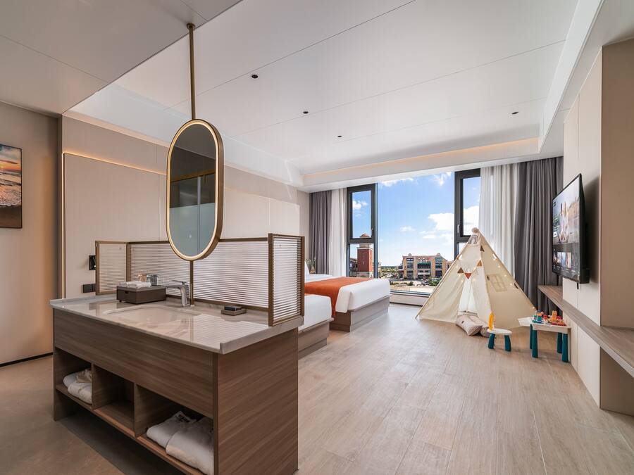 A modern hotel room with a large mirror, a wooden vanity, a bed with a view, a tent, and a flat-screen TV.