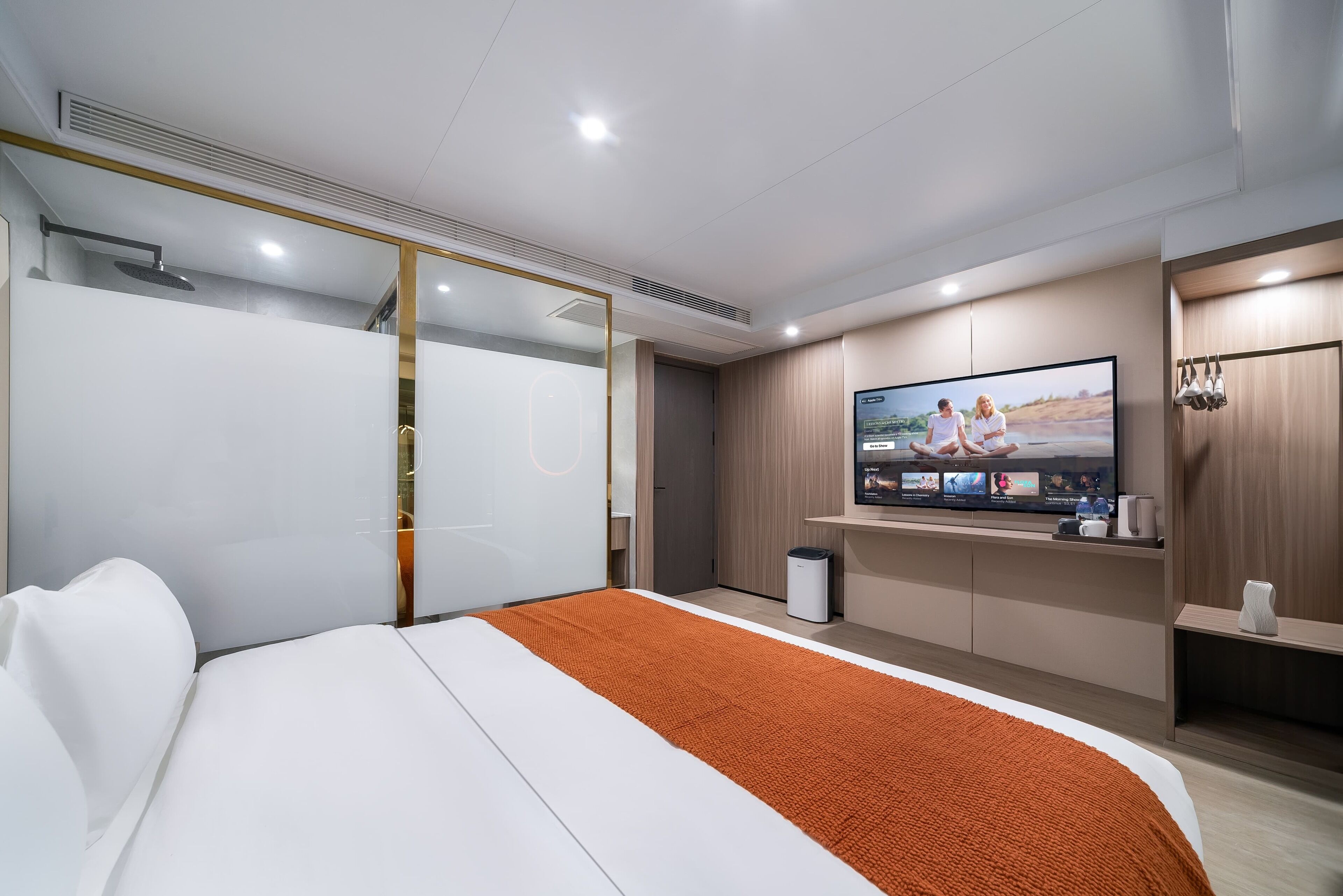 A modern hotel room with a large bed, a television mounted on the wall, and a wooden cabinet.