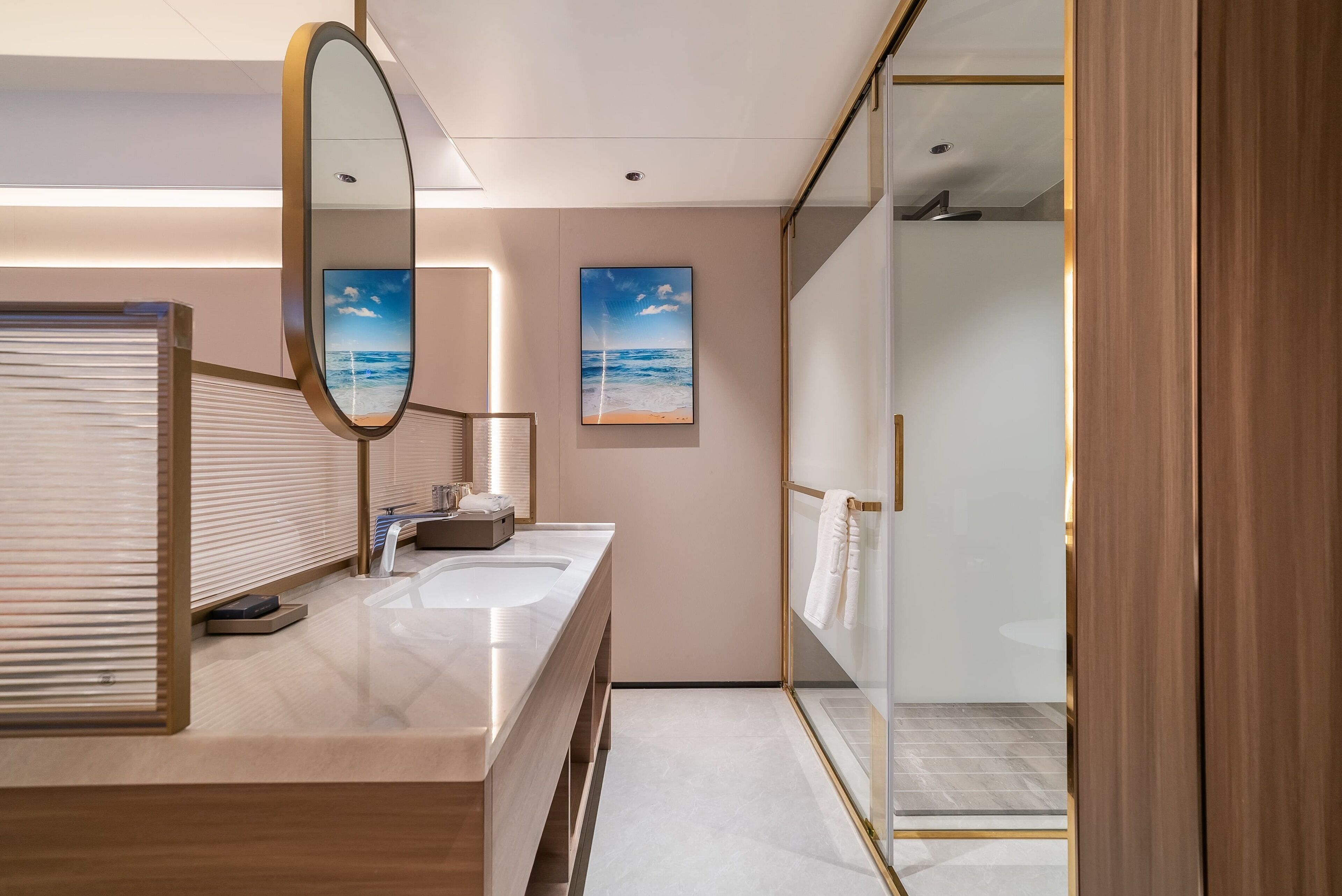 A modern bathroom with a large mirror, two sinks, a towel rack, and a framed beach picture on the wall.