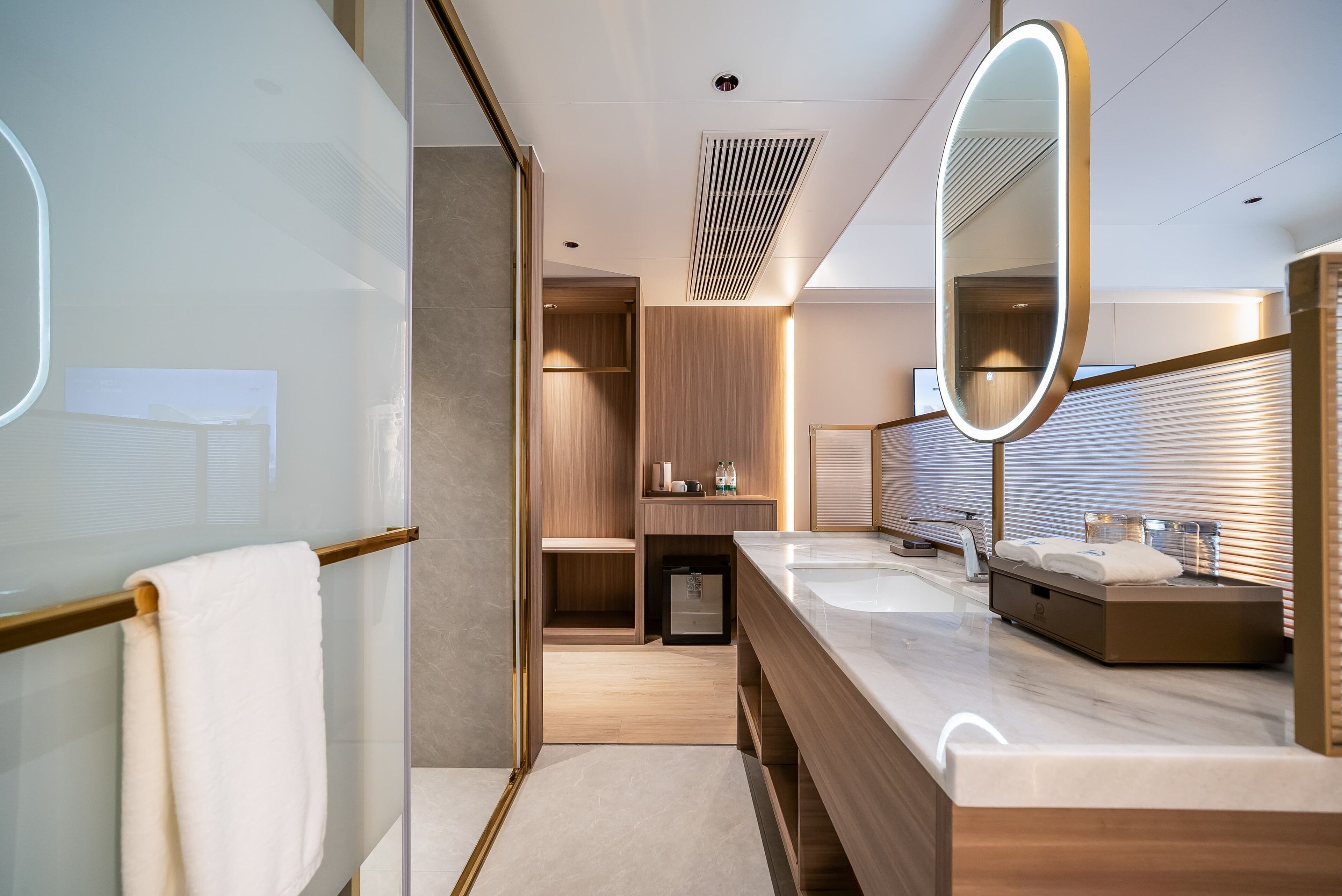 Een moderne badkamer met glazen douchewand, houten wastafelmeubel, dubbele wastafels en een grote spiegel.