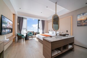 Una habitación de hotel moderna con una cama grande, una zona de estar con una mesa y sillas, un baño con un espejo amplio y un televisor montado en la pared.