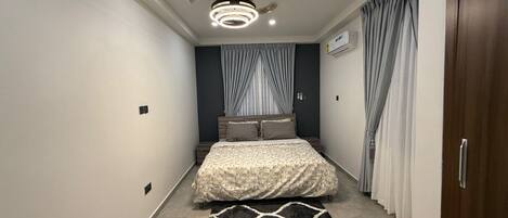 Une chambre à coucher comprenant un lit, un ventilateur de plafond, des spots encastrés, un tapis et des rideaux.
