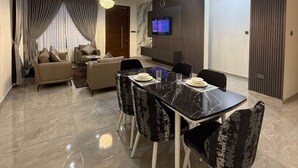 A modern living room with a dining area, featuring a marble floor, a chandelier, a sofa set, and a television mounted on the wall. - fransons Homes (Tema)