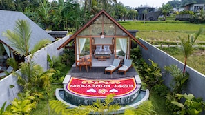 A modern villa with a glass-enclosed bedroom, a circular flower bed with 'HAPPY HONEYMOON' written on it, and a lush garden surrounding the property. - The Udiana Ubud  (Tegallalang)