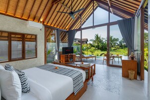 Un dormitorio con cama, televisor, escritorio y vista a un jardín.