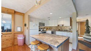 A modern kitchen with granite countertops, white cabinets, and a central island with stools. - 4 bedroom 3 bath ski in ski out townhome seven springs mountain resort!! (Champion)