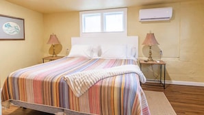 Un dormitorio con una cama, dos lámparas de noche, un ventanal, aire acondicionado y un cuadro en la pared.