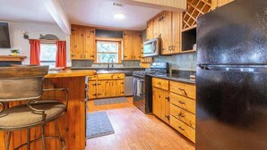 A kitchen with wooden cabinets, a black refrigerator, a microwave, and a bar stool. - The Bear’s Den at Triple Z (Medicine Park)