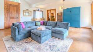 A living room with a sectional sofa, a patterned rug, a wooden door, and a blue cabinet. - The Bear’s Den at Triple Z (Medicine Park)