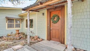 A house with a wooden porch, a front door with a wreath, and a stone pathway leading to the door. - The Bear’s Den at Triple Z (Medicine Park)