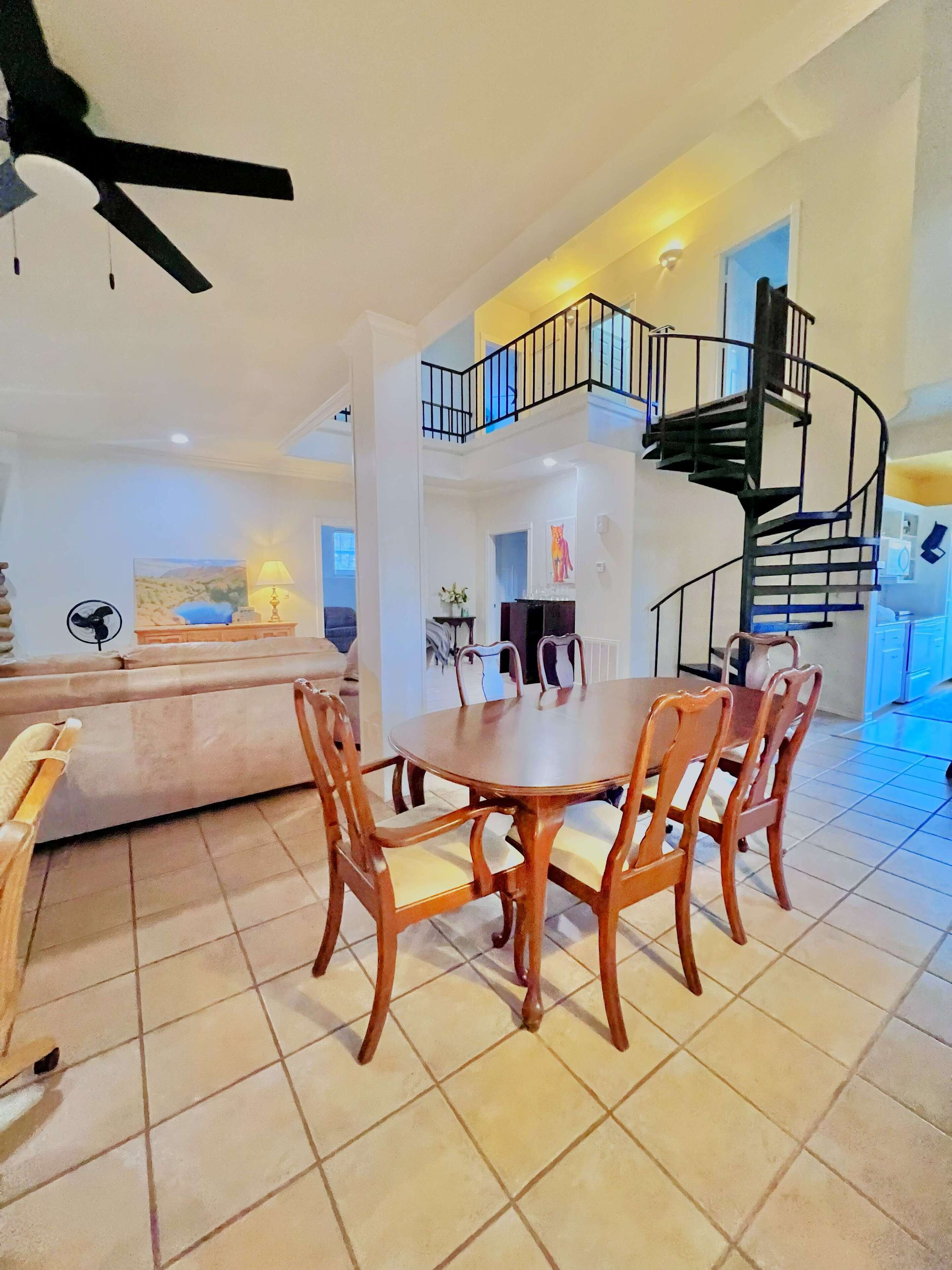 Un vaste espace de vie comprenant une table et des chaises, un escalier et un ventilateur de plafond.