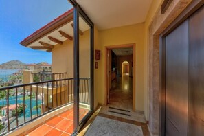 A balcony with a view of a pool and mountains, a door leading to an interior space, and a tiled floor. - Cabo Oceanfront 3BR Penthouse 3,000 Sq Ft  Private Hot Tub (Cabo San Lucas)