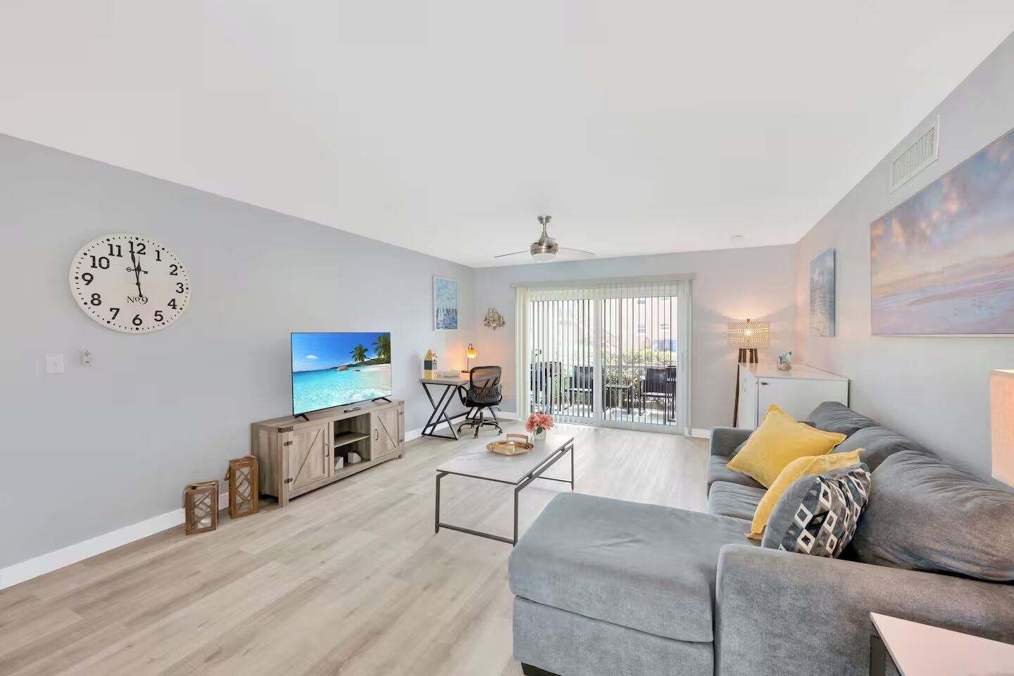 Een moderne woonkamer met een flatscreen televisie, een grijze bank, een salontafel en een houten kast.