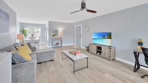 Ett modernt vardagsrum med en grå soffa, ett soffbord och en tv-skärm som visar en strandvy.