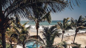 A beach view with palm trees, a pool, and a clear sky. - Peña Linda Bungalows (Los Organos)