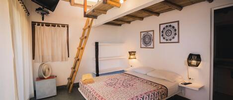 Un dormitorio con cama, mesitas de noche, un ventilador, una escalera, televisión y ventilador de techo.