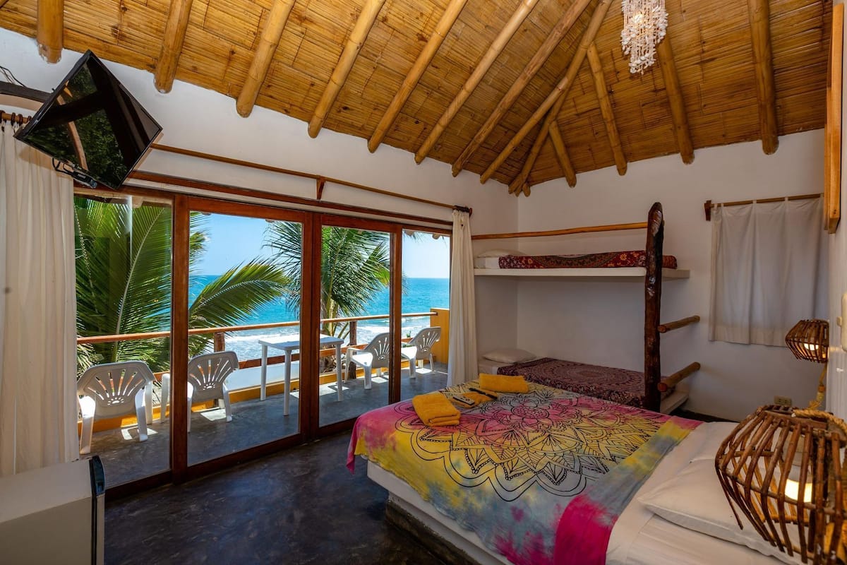 Ein Zimmer mit einem Bett, Etagenbetten, einem Balkon mit Stühlen, einem Fernseher und Blick aufs Meer.