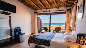 A bedroom with a bed, a TV, a fan, and a view of the beach. - Peña Linda Bungalows (Los Organos)