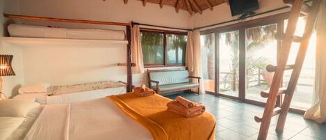 Una habitación con cama, banco, televisor y vistas al exterior.