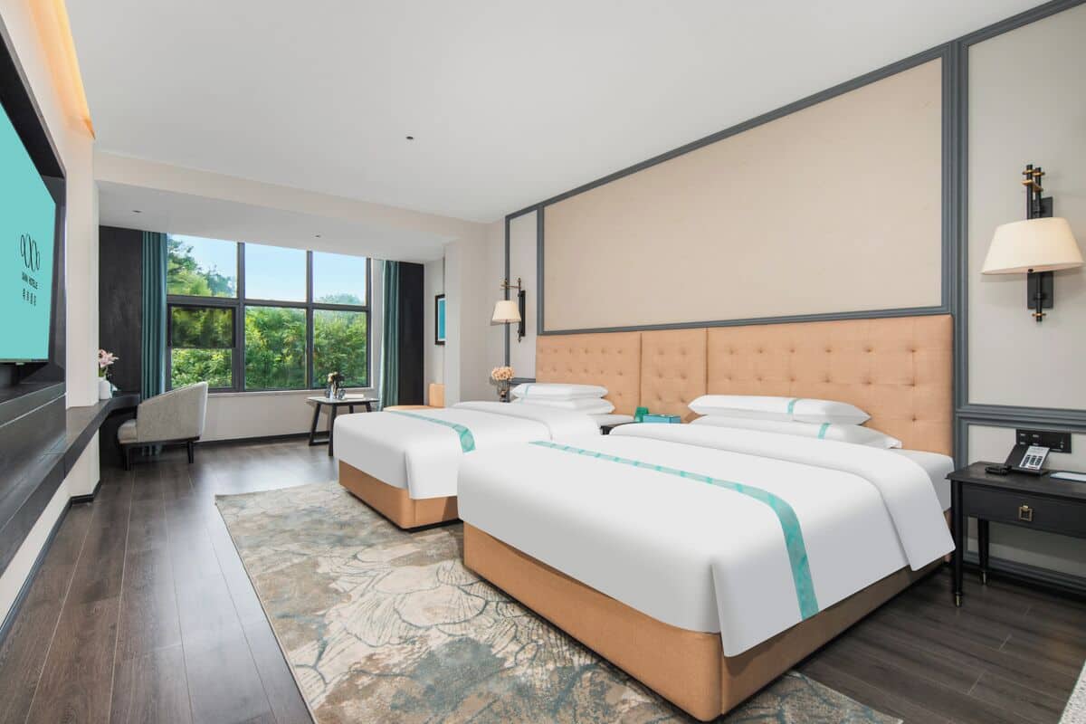 Habitación de hotel con dos camas, un ventanal grande, un escritorio y una silla.