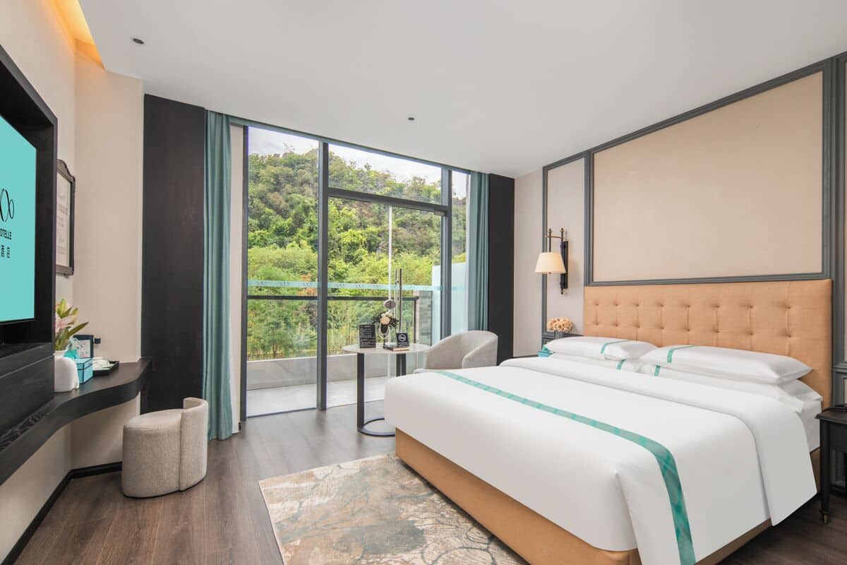 Habitación de hotel moderna con una cama grande, televisión, escritorio y vistas a zonas verdes.