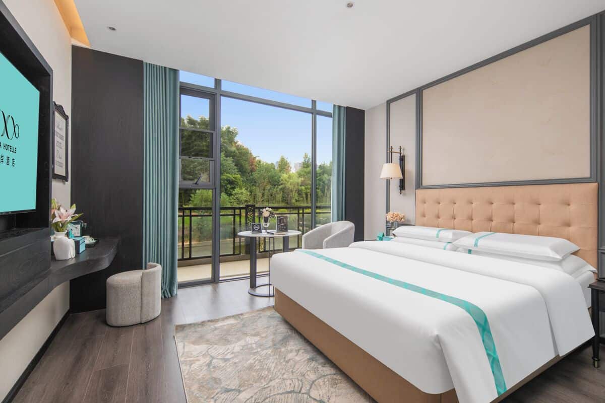 Habitación de hotel con una cama grande, televisión, balcón con vistas y escritorio con lámpara.