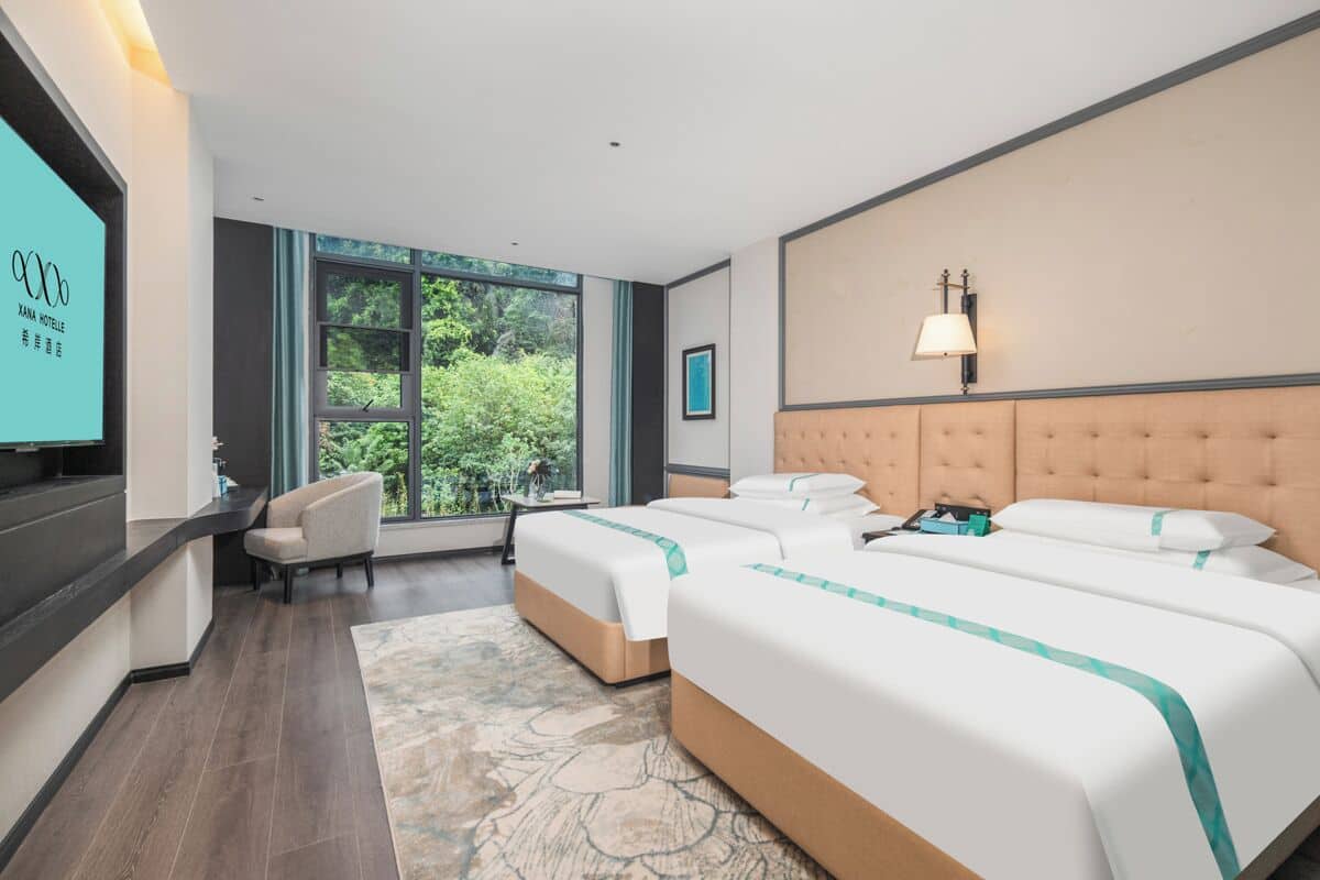 Habitación de hotel con dos camas, un sofá, una televisión y una ventana con vistas a zonas verdes.