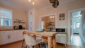 A kitchen with white cabinets, a wooden table, wicker chairs, a microwave, and a chandelier. - Downtown Heritage Home | 3 Bed + Backyard (St. John`s)
